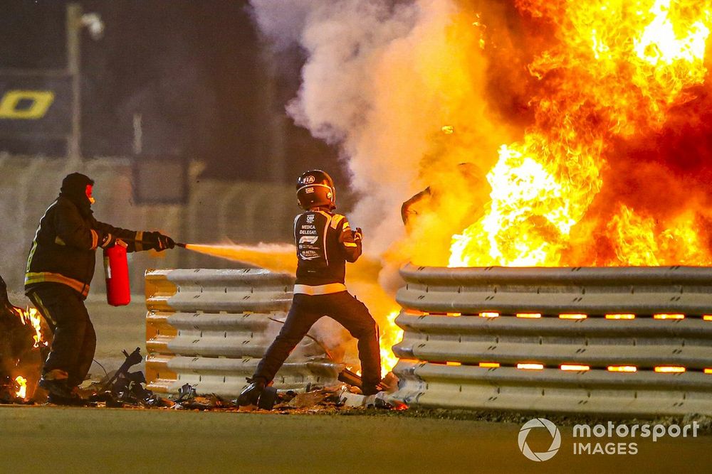 Fire marshals deal with the flames and a medical delegate assists Romain Grosjean, Haas F1, after a huge crash on the opening lap